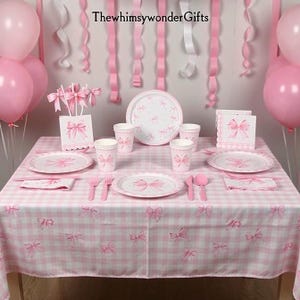 May include: A party table setting with a pink and white gingham tablecloth featuring bow patterns. The set includes paper plates, cups, and napkins decorated with pink bows, pink plastic cutlery, and pink balloons. Text reads ThewhimsywonderGifts.