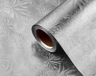 May include: A roll of silver wallpaper with a repeating floral pattern. The wallpaper is partially unrolled, revealing the pattern and the brown cardboard core. The design features stylized flowers and leaves.