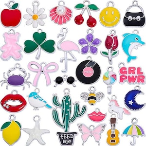 May include: A collection of colorful enamel charms in various shapes, including a red apple, a daisy, a pink flamingo, a smiley face, a shamrock, a dolphin, a cactus, a butterfly, and a guitar. Each charm has a silver-tone loop for attaching to jewelry or crafts.