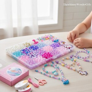 May include: A clear plastic organizer filled with colorful beads in various shapes and sizes. Several beaded necklaces and bracelets are displayed, along with a pink box, scissors, and spools of string. The text "ThewhimsyWonderGifts" is visible in the top right corner.