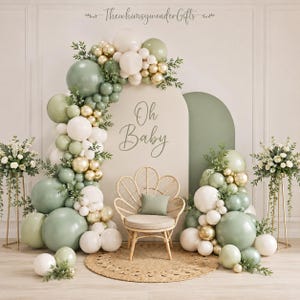 May include: A decorative event display featuring a large arch backdrop with the text Oh Baby, a rattan chair with a sage green cushion, and an organic balloon garland in sage green, white, and metallic gold, accented with green foliage.