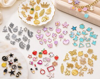 May include: A collection of various charms in gold, silver, and colorful enamel. The charms include stars, hearts, butterflies, crowns, and other decorative shapes. Some charms are on a white plate, while others are scattered on a white surface.