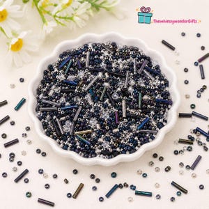 May include: A white, scalloped-edge bowl filled with a mix of small, dark blue beads, silver beads, and iridescent tube beads. Scattered around the bowl are additional beads. The Whimsy Wonder Gifts logo is in the top right corner.