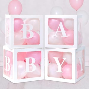 May include: Four white, square boxes spelling "BABY" with large, white letters. Each box has clear sides and is filled with pink and white balloons. Pink balloons are also floating above the boxes, creating a festive display.