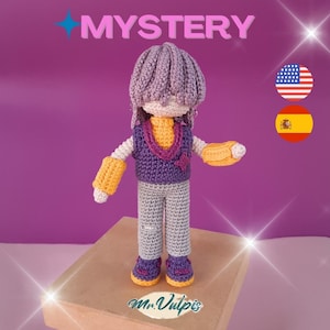 Puede incluir: Muñeca de ganchillo hecha a mano con sombrero, chaleco y zapatos morados, y pantalones grises. La muñeca tiene detalles amarillos en las mangas y un cuello amarillo. La palabra "MYSTERY" está arriba.