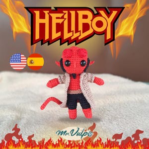 Op de afbeelding: Gehaakte Hellboy-pop met een rode body, zwarte korte broek en een beige jas. De pop heeft zwarte ogen en kleine hoorns. Het woord "HELLBOY" wordt in rood en geel weergegeven. De tekst "Mr. Vulpis" is ook aanwezig.