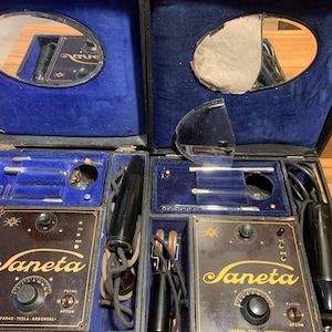 May include: A vintage medical device kit in a black case with blue velvet lining. The kit contains various tools, two control panels with the name "Saneta", and two mirrors. The case is open, displaying the contents.