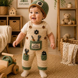 May include: A beige and green crocheted overall set with a matching beanie. The overalls feature a front pocket with the text "LITTLE MECHANIC" and small tool-shaped appliques. The beanie has a matching green and beige color scheme.