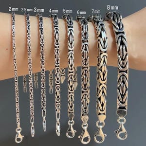 May include: A collection of eight silver-toned Byzantine chain bracelets arranged by width, labeled from 2 mm to 8 mm. Each bracelet features a complex, interlocking woven metal link pattern and a polished lobster claw clasp at the bottom end.
