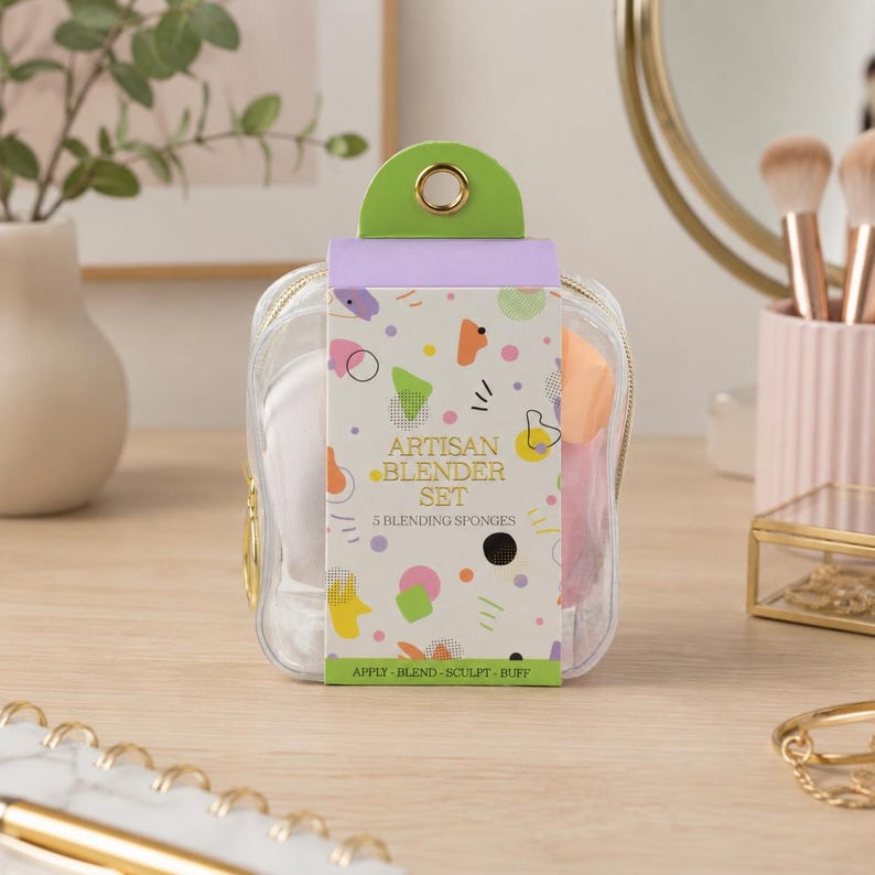 K&ouml;nnte beinhalten: Eine transparente Kosmetiktasche mit einem gr&uuml;nen und goldenen Griff enth&auml;lt ein Set aus f&uuml;nf Make-up-Schw&auml;mmen. Die Verpackung tr&auml;gt den Text "ARTISAN BLENDER SET" und bunte geometrische Formen. Auf der Unterseite der Verpackung steht "APPLY - BLEND - SCULPT - BUFF."