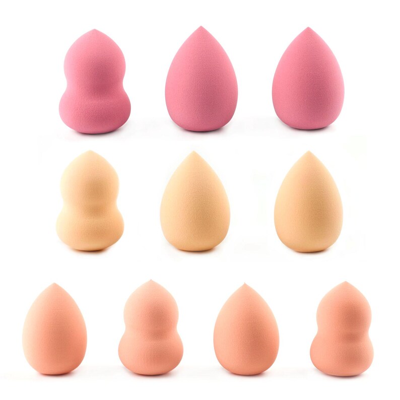 May include: A collection of ten makeup sponges arranged in three rows. The sponges come in various shades of pink, peach, and beige. Some sponges have a classic teardrop shape with a pointed tip, while others feature a contoured hourglass shape.