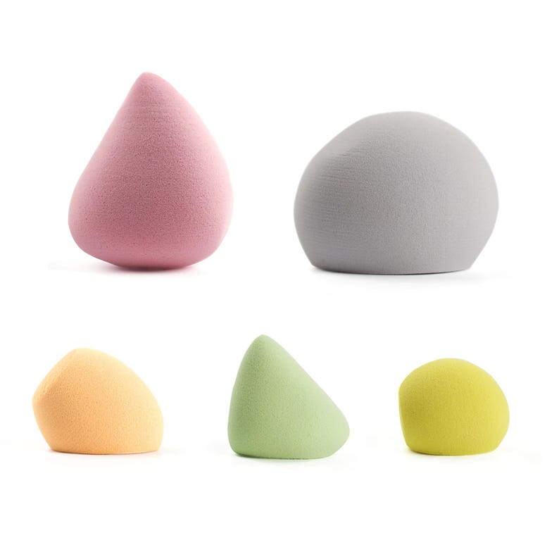K&ouml;nnte beinhalten: F&uuml;nf farbige Make-up-Schw&auml;mme in verschiedenen Formen. Die Schw&auml;mme sind in den Farbt&ouml;nen Rosa, Grau, Orange, Gr&uuml;n und Gelb gehalten. Die Formen umfassen eine Tr&auml;ne, eine abgerundete Form, einen Keil und eine abgerundete Form.