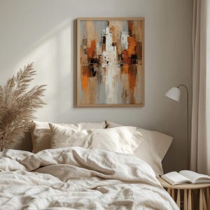 May include: Abstract cityscape painting in a wooden frame. The artwork features a palette of orange, white, gray, and brown hues, creating a modern and artistic aesthetic. The painting is displayed above a bed with neutral-toned bedding.
