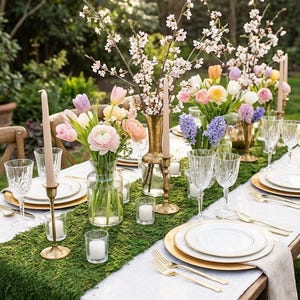 May include: A beautifully set outdoor dining table with a moss runner, white plates, gold chargers, and elegant glassware. Floral arrangements of tulips, hyacinths, and cherry blossoms adorn the table, along with candles in gold holders, creating a festive atmosphere.