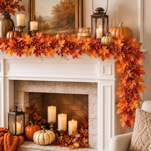 May include: An artificial autumn garland featuring vibrant orange and red maple leaves and small red berries draped across a white fireplace mantel, accented by various pumpkins, lit candles in glass holders, and metal lanterns.