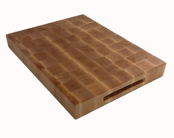 May include: A rectangular end-grain butcher block cutting board. The board is made of light brown wood with a checkerboard pattern. It features a recessed handle on one side for easy carrying. This kitchen item is ideal for food preparation.