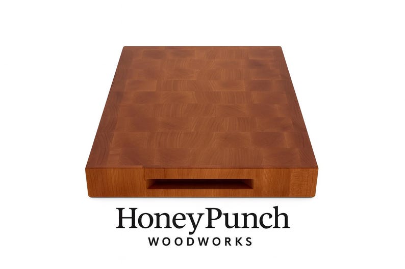 May include: A rectangular, end-grain wooden cutting board with a warm brown hue. The board features a built-in handle and the text "HoneyPunch WOODWORKS" in black. The wood grain pattern is visible across the surface.