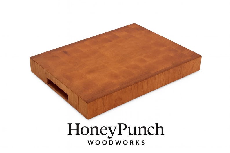 May include: A rectangular, end-grain cutting board made of light brown wood. The board has a handle cutout on one side and the HoneyPunch Woodworks logo at the bottom. The wood grain pattern is visible on the surface.