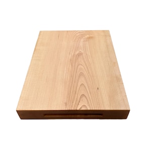 May include: A rectangular wooden cutting board with a light brown finish. The wood grain is visible across the surface. A recessed handle is cut into one of the shorter sides.