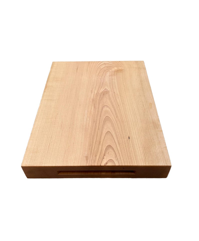 May include: A rectangular wooden cutting board with a light brown finish. The wood grain is visible across the surface. A recessed handle is cut into one of the shorter sides.