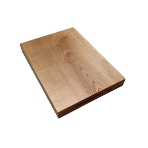May include: A rectangular wooden cutting board with a light brown finish. The board has a natural wood grain pattern and a recessed handle on one side. The cutting board is made of solid wood.