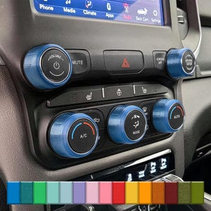 Könnte beinhalten: Blaue Innenraum-Bedienknöpfe für Autos mit weißem Text und Symbolen. Die Knöpfe steuern Lautstärke, Stummschaltung, Klimaanlage, Modus und Automatikfunktionen. Das Armaturenbrett hat auch einen Bildschirm und verschiedene Tasten.