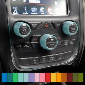 May include: Teal-colored car control knobs with silver accents. The knobs are on a black dashboard with buttons for radio, media, and climate control. The image also shows a color palette of various shades.