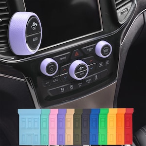 May include: A car interior with light purple control knobs and a matching air vent cover. The knobs have black text and icons. Below are several colored rectangular car key covers.