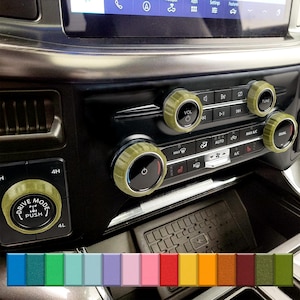 May include: Olive green car interior control knobs and buttons. The knobs are textured and surround the buttons for volume, tuning, and climate control. A row of color swatches is at the bottom.