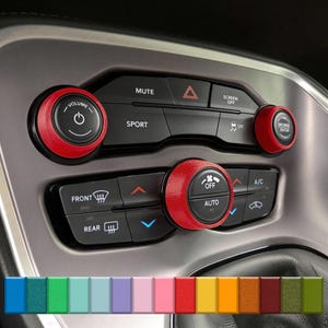 Könnte beinhalten: Auto-Innenraum mit roten Akzentknöpfen. Die Knöpfe befinden sich um die Lautstärke-, Klima- und Bildschirmfunktionen. Die Knöpfe sind schwarz mit weißem Text. Das Armaturenbrett des Autos ist grau.