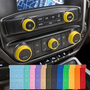 May include: Yellow control knobs on a black car dashboard. The knobs are circular with black centres and are labelled with various functions. Below the dashboard are several coloured door handle protectors.