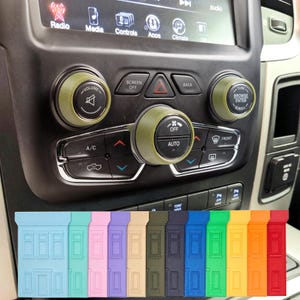May include: Olive green car control knob covers and a variety of colorful rectangular car key covers. The car control knobs are on a black dashboard. The key covers are in shades of blue, pink, purple, beige, green, navy, blue, green, yellow, orange, and red.
