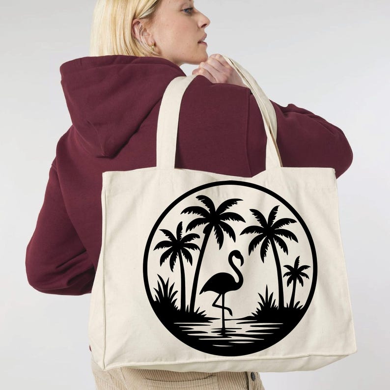May include: Cream-colored tote bag featuring a black circular design with a flamingo, palm trees, and water. The bag has two long handles and is made of a sturdy fabric, perfect for carrying groceries or personal items.
