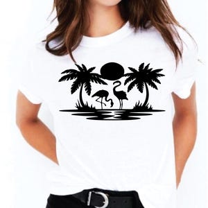 May include: White t-shirt featuring a black graphic of two flamingos, palm trees, and a sun over water. The design is centered on the shirt. The shirt has short sleeves and a crew neck.