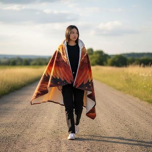 May include: A hooded cloak with a vibrant design of orange, red, and yellow hues, resembling a sunset or flames. The cloak is worn by a person walking on a gravel road, surrounded by fields of tall grass under a cloudy sky.