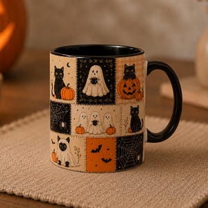 May include: A ceramic mug with a black handle and interior, featuring a patchwork-style Halloween print. The design includes illustrations of black cats, ghosts, pumpkins, spiderwebs, and bats in orange, black, and cream colours.