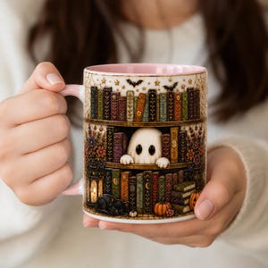 May include: A ceramic mug with a light pink interior and handle, featuring a detailed illustration of a bookshelf filled with colorful books, a white ghost peeking out from the shelves, a black cat, pumpkins, and a lantern with a glowing light.