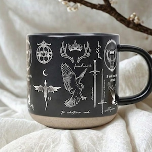 May include: Black ceramic mug with a black handle and a tan base. The mug is decorated with white illustrations of a crown, swords, a dragon, and other symbols. Text includes "To whatever end" and "I will not be afraid."