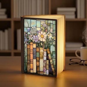 May include: A decorative book-shaped lamp with a stained-glass panel featuring flowers and books. The lamp has a warm glow, with the pages illuminated. The stained-glass panel showcases a variety of colorful flowers and books, creating a cozy and artistic ambiance.
