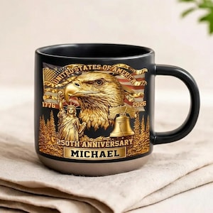 May include: Black ceramic mug with a gold design featuring an eagle, American flag, and the Statue of Liberty. The mug commemorates the 250th anniversary and includes the name "MICHAEL".