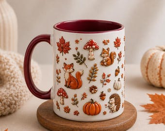 May include: A white ceramic mug with a deep red interior and handle, featuring a repeating pattern of orange foxes, hedgehogs, squirrels, red and white mushrooms, pumpkins, acorns, and autumn leaves in shades of brown, orange, and red.