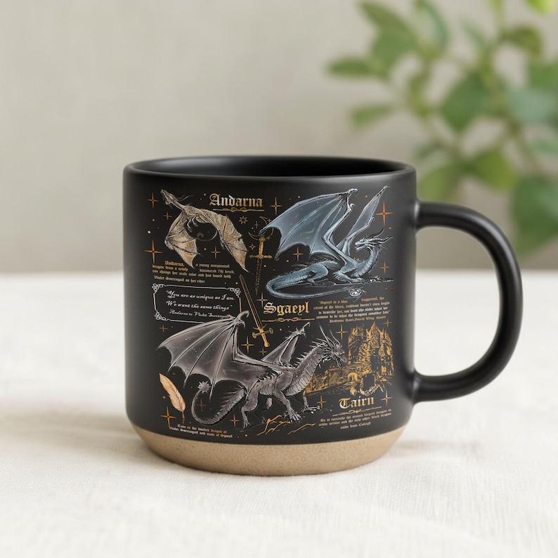 May include: Black ceramic mug with a tan base, featuring illustrations of dragons and text. The dragons are in various poses with different wing designs. The mug has a black handle and the text includes the names "Andarna", "Sgaeyl", and "Tairn".