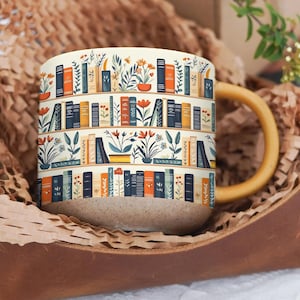 May include: A ceramic coffee mug with a tan base and a yellow handle. The mug features a repeating pattern of bookshelves with books, plants, and flowers in orange, blue, and yellow. The mug is presented in a brown leather container with brown paper.