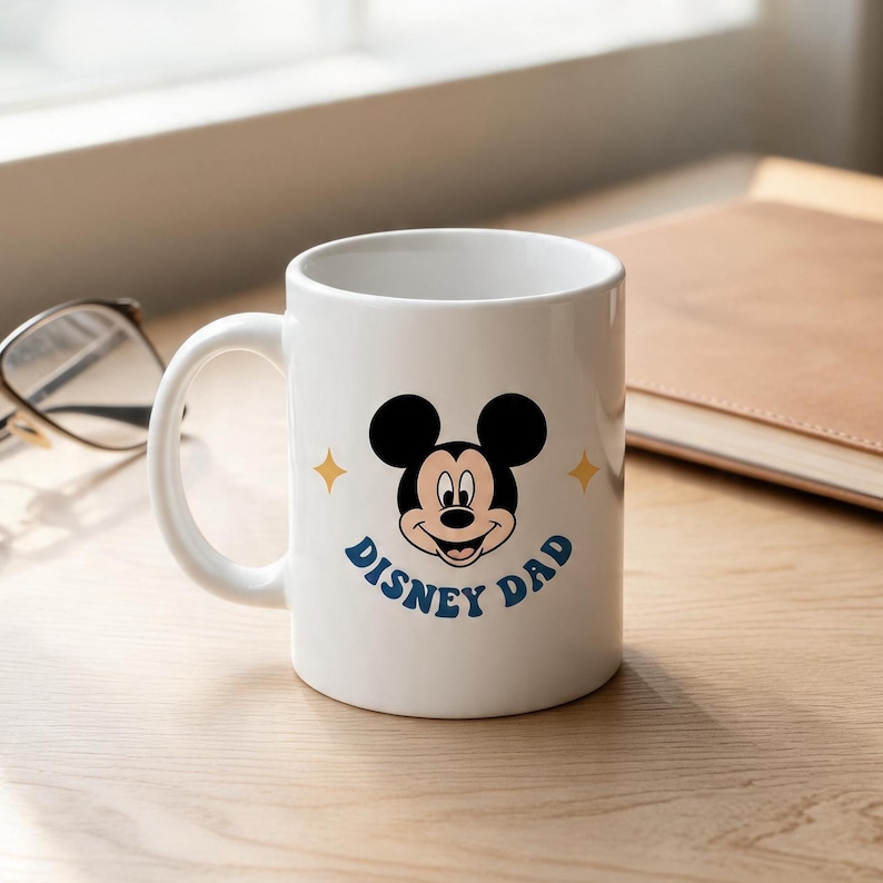 Puede incluir: Una taza de cer&aacute;mica blanca con un gr&aacute;fico del rostro de Mickey Mouse centrado en el frente. Debajo del personaje, el texto "DISNEY DAD" aparece en letras may&uacute;sculas azules. Dos peque&ntilde;as estrellas amarillas de cuatro puntas flanquean las orejas.