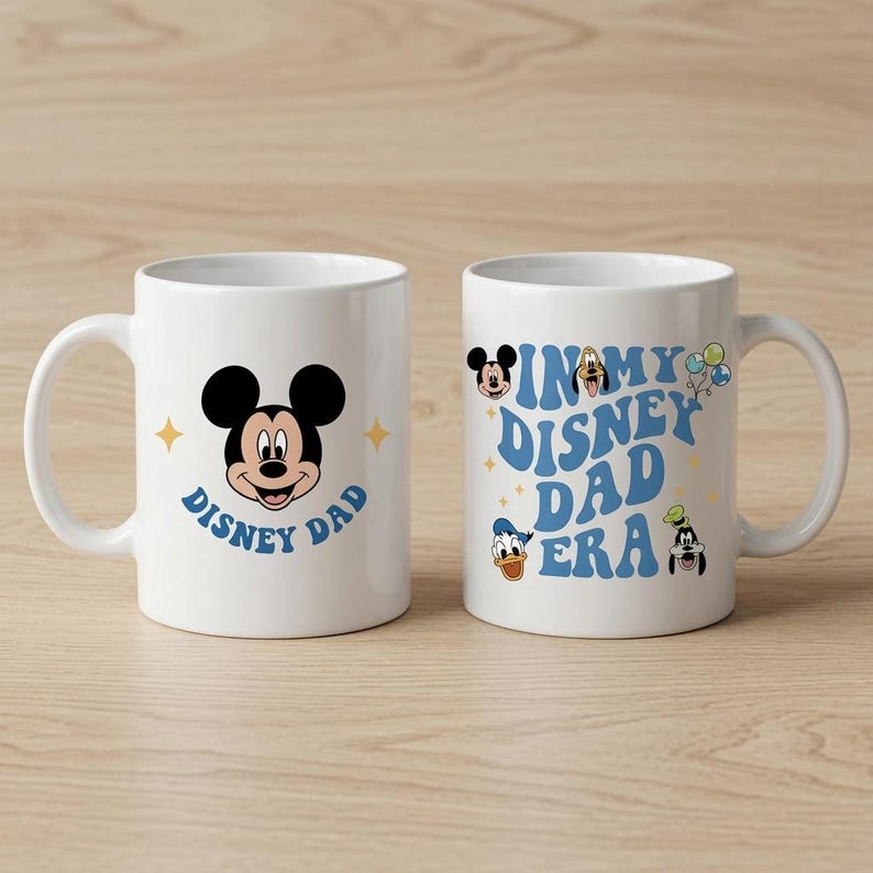 Puede incluir: Dos tazas de cer&aacute;mica blanca con gr&aacute;ficos de personajes de Disney. La taza izquierda muestra a Mickey Mouse con el texto "DISNEY DAD". La taza derecha muestra el texto "IN MY DISNEY DAD ERA" rodeado por cabezas de Mickey, Pluto, Donald y Goofy.
