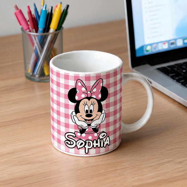 Puede incluir: Una taza de cer&aacute;mica blanca con un patr&oacute;n de cuadros vichy en rosa y blanco. El frente muestra un gr&aacute;fico de Minnie Mouse con un lazo de lunares, con el nombre Sophia impreso en letras cursivas negras debajo de la ilustraci&oacute;n.