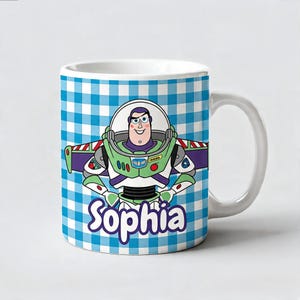 May include: A white ceramic mug featuring a blue and white checkered pattern background. The center displays a cartoon illustration of a space ranger character in a green, white, and purple suit. The name Sophia is printed in purple below.