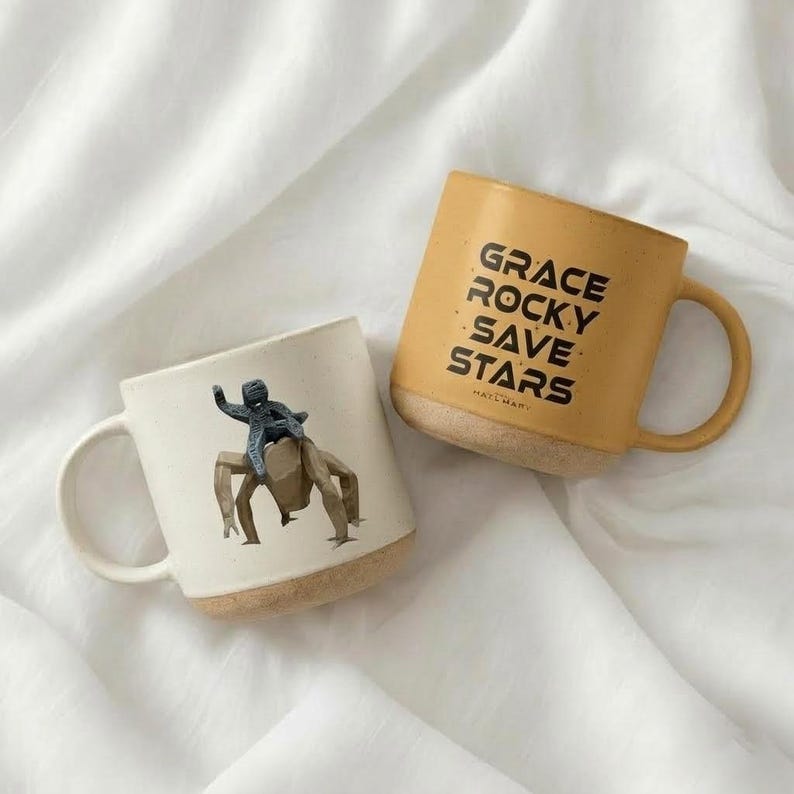 May include: A set of three ceramic mugs with a speckled, cream-colored glaze. Each mug features a different hand-painted floral design in shades of blue, green, and yellow. The mugs have a simple, rounded shape and a comfortable handle.