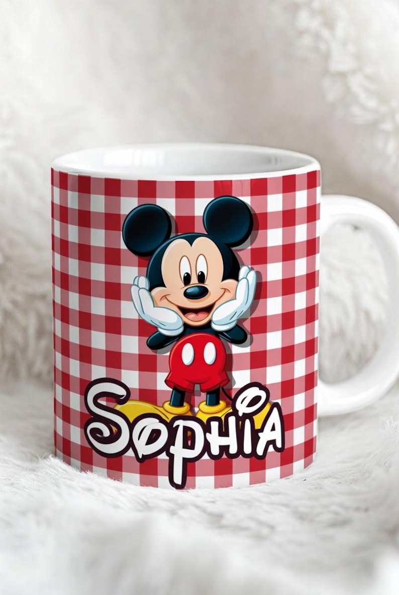 K&ouml;nnte beinhalten: Ein wei&szlig;er Keramikbecher mit einem rot-wei&szlig;en Vichy-Karo-Muster. Der Becher zeigt eine Grafik von Mickey Mouse mit den H&auml;nden an den Wangen, platziert &uuml;ber dem Namen Sophia, der in einer stilisierten wei&szlig;en Schrift mit schwarzem Rand steht.