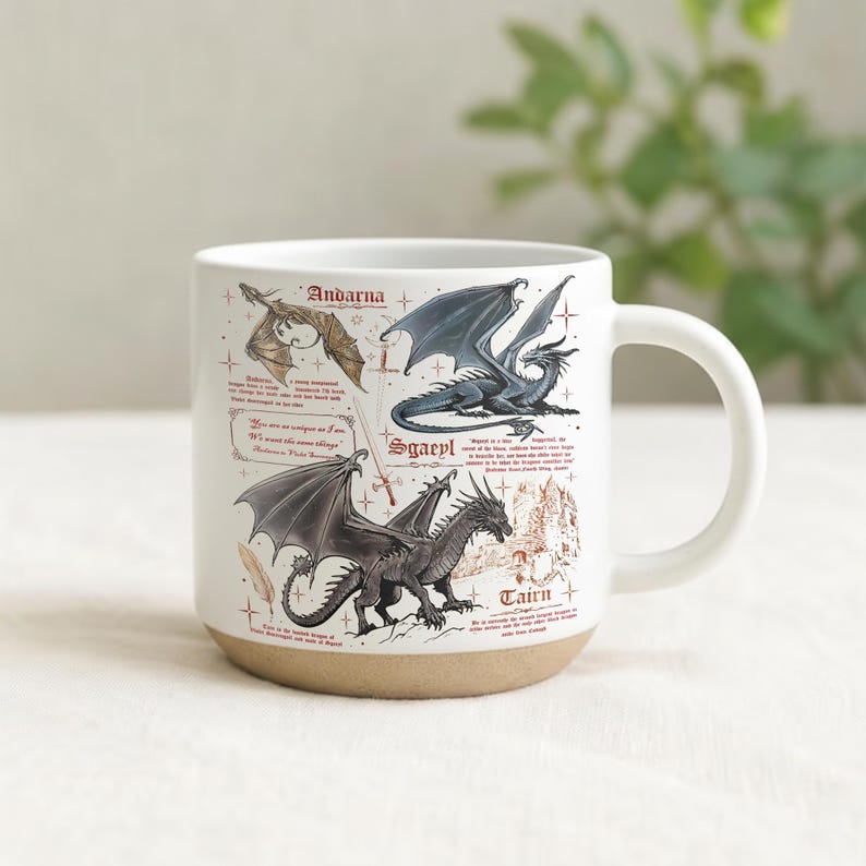May include: White ceramic mug with a tan base, featuring illustrations of three dragons with names: Andarna, Sgaeyl, and Tairn. The mug has a curved handle and includes text descriptions of each dragon. The background is a soft, neutral color.